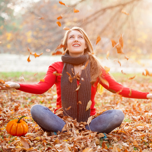 Woman with her hands in the air with leaves falling and a pumpkin next to her. Fall Fashion trends on the g bond